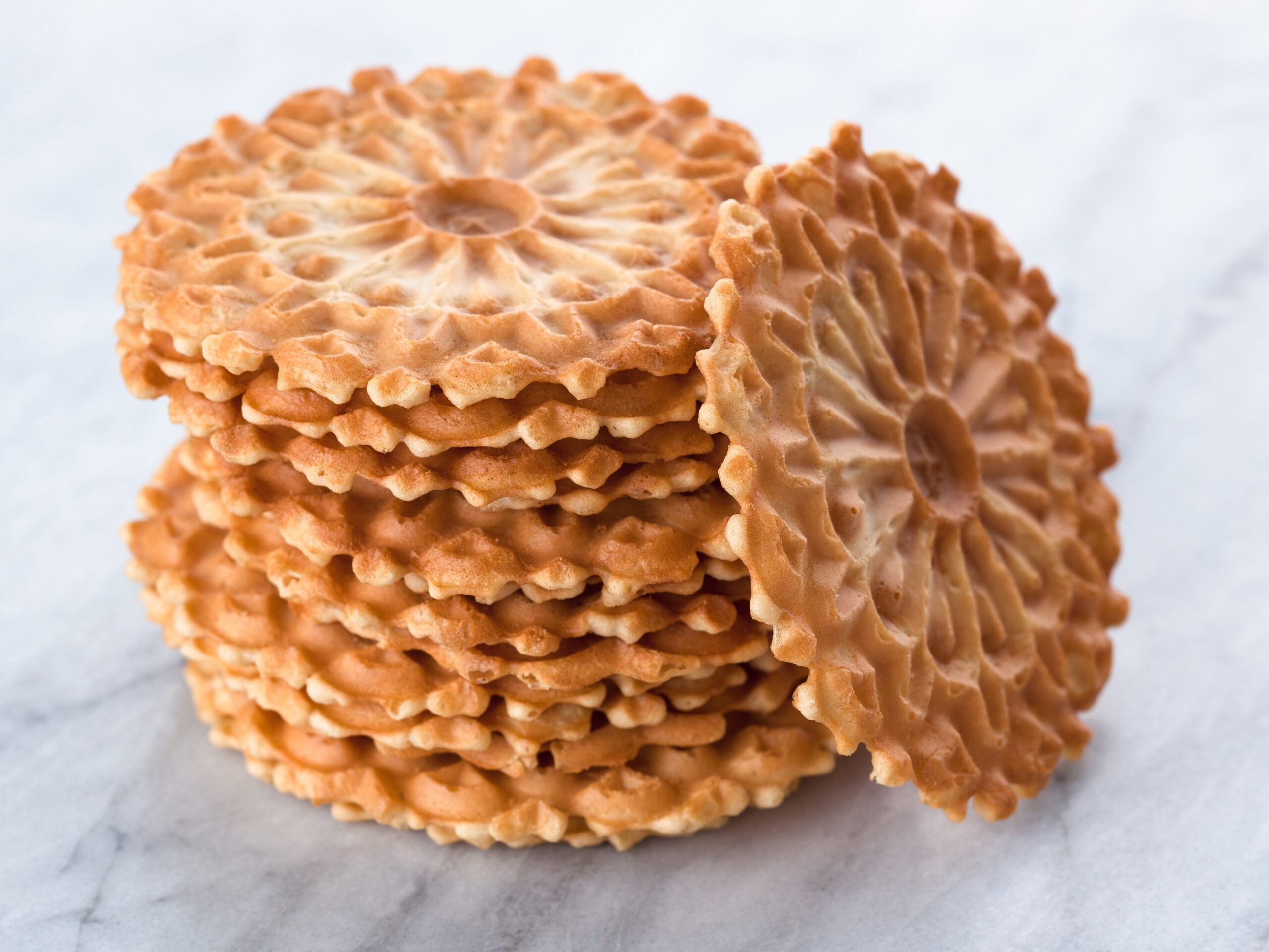 Studio photo of stack of traditional Italian cookies commonly called "pizzelles" on white marble