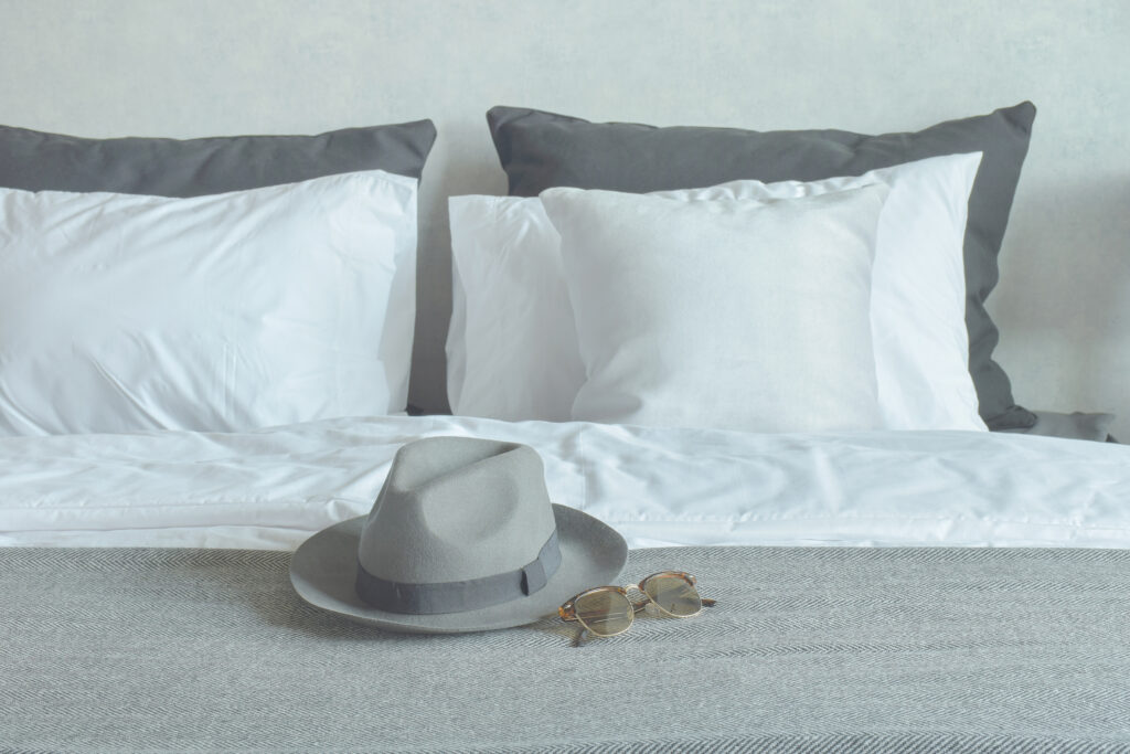 Man's hat and sunglasses on a bed.