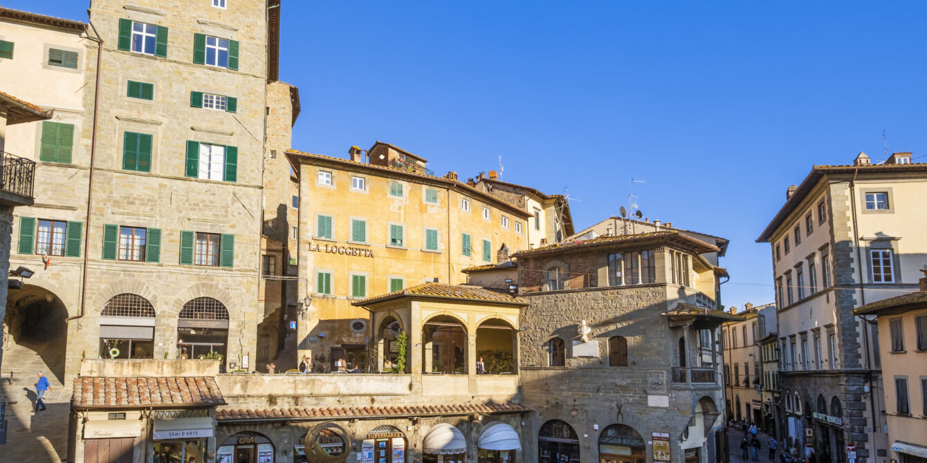 People strolling in the Piazza della Repubblica, the core of the old town of Cortona, bounded by historic buildings such as the Palazzo del Capitano del Popolo, dating back to the 13th century